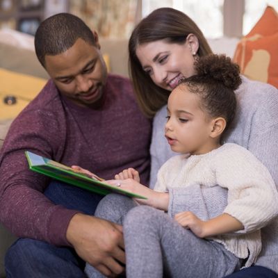 Image of parents reading together with a child. Everyone is engaged with reading. 