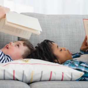 Two children laying on a sofa reading books
