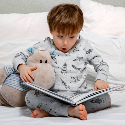 Boy holding a toy hippo and looking shocked about the book he is reading