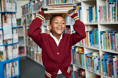 girl carrying books over her head in a library